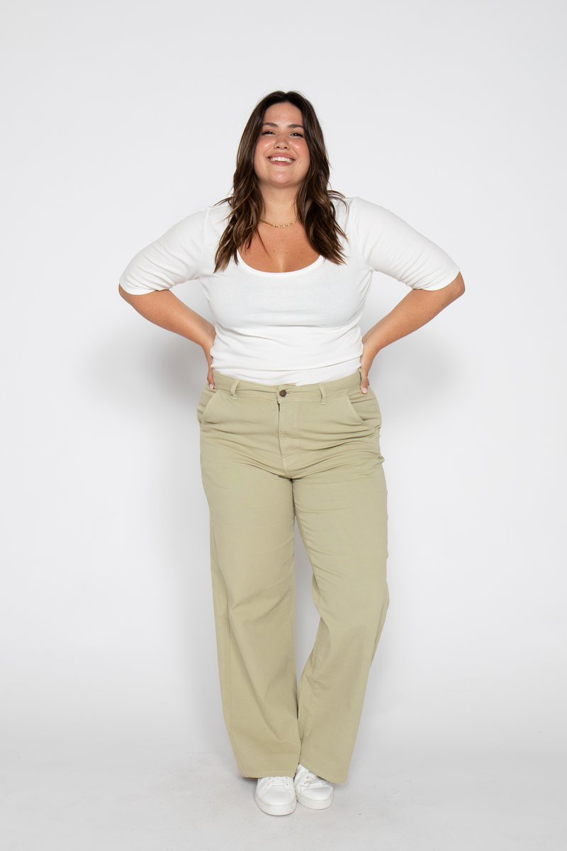 Plus-size woman in high-rise flare pants, standing confidently with hands on hips, wearing a white top and sneakers.