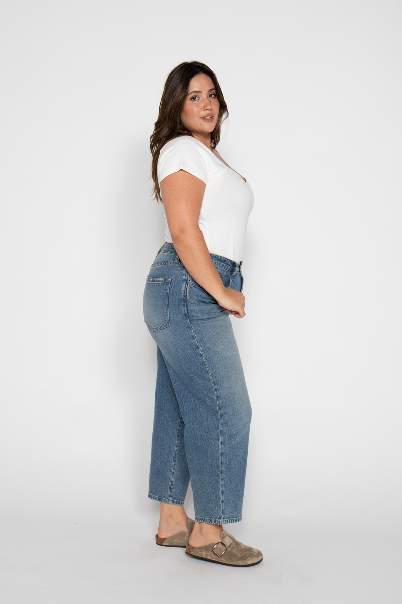 Side view of plus-size model in high rise wide leg crop jeans, paired with casual shoes, showcasing the vintage cropped denim.