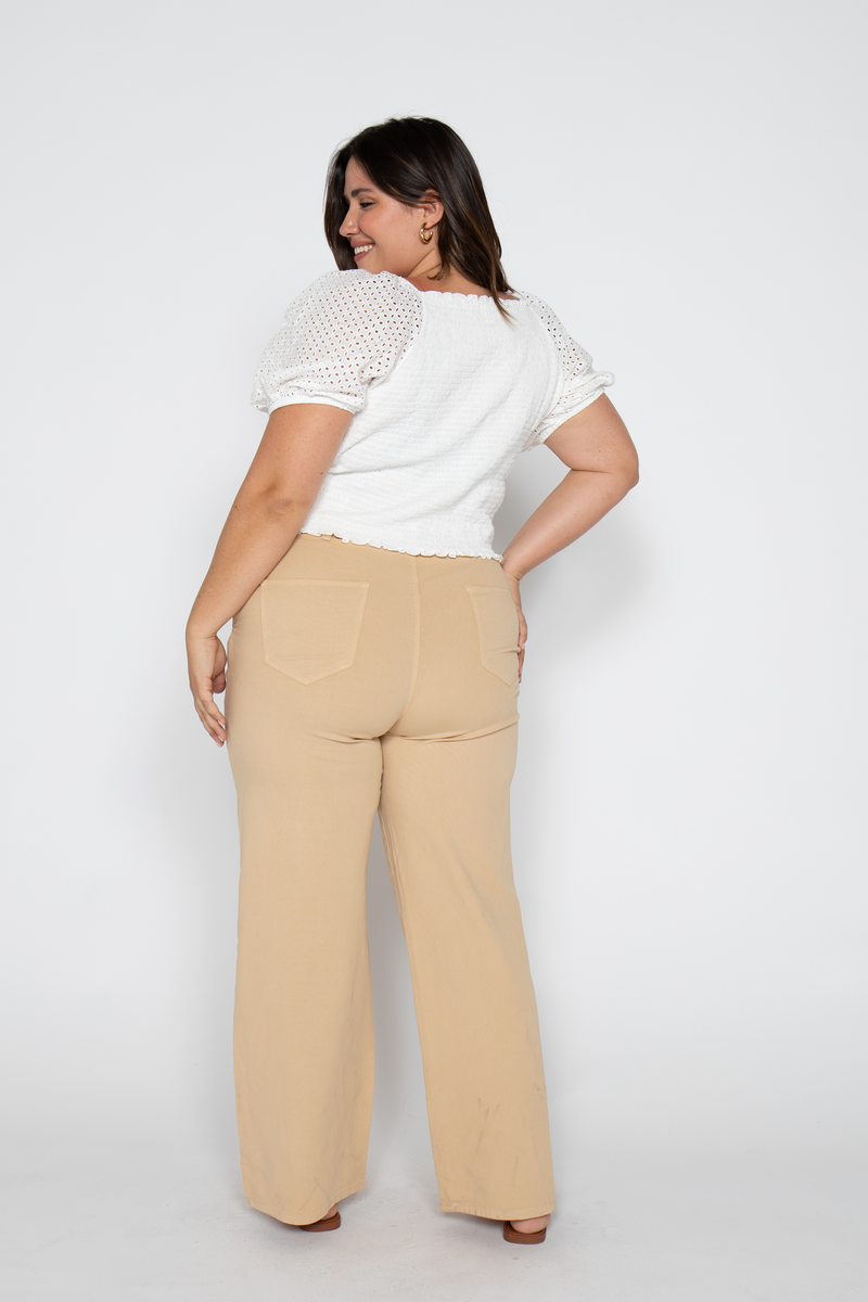 Back view of plus-size model in beige wide-leg trousers paired with a white puff-sleeve top.
