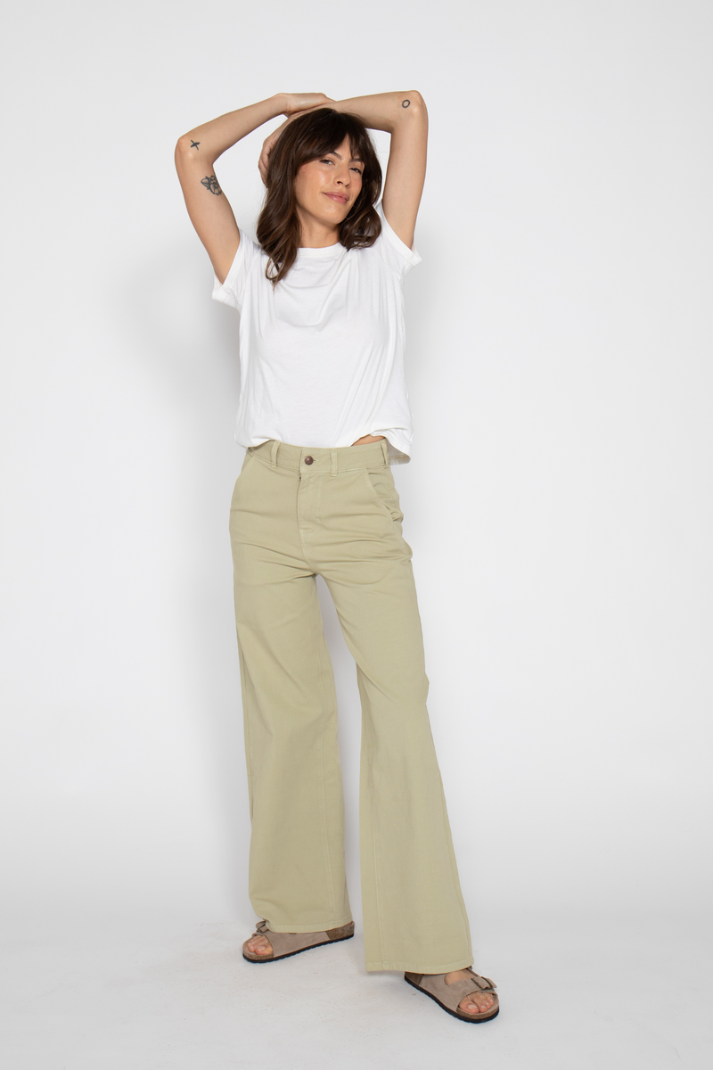 Woman adjusts hair, wearing lightweight high-waisted flare pants, standing in a relaxed pose with hands in pockets.