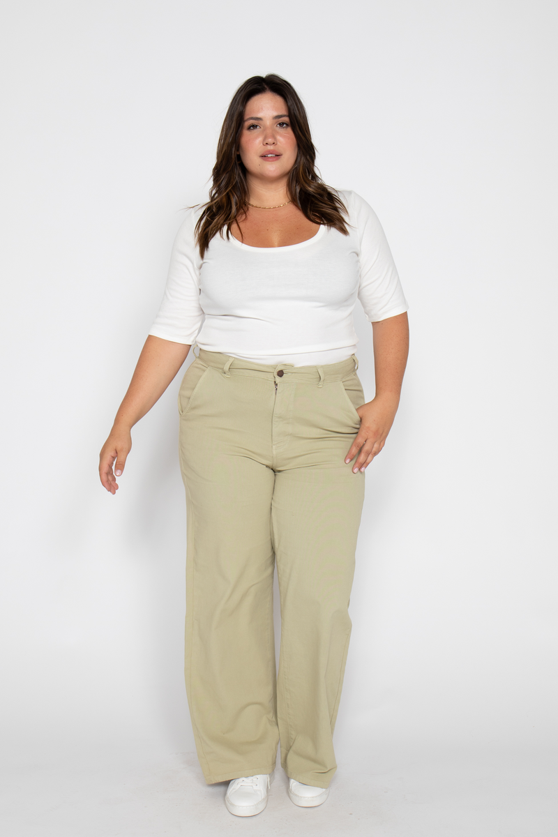 Plus-size woman walking in high-rise flare pants, standing sideways in a relaxed pose, wearing casual white sneakers.