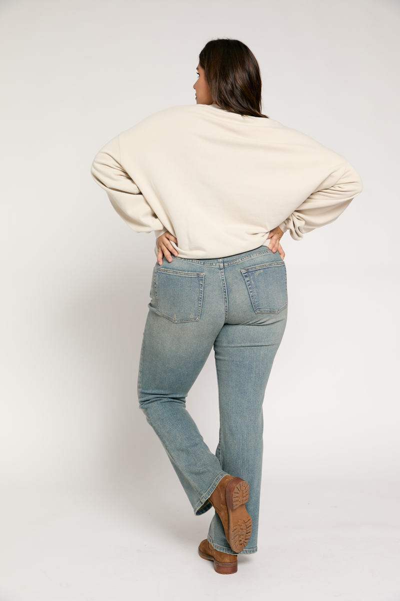 Plus-size model in a side pose wearing light vintage wash jeans, showing the comfortable fit and versatile style.