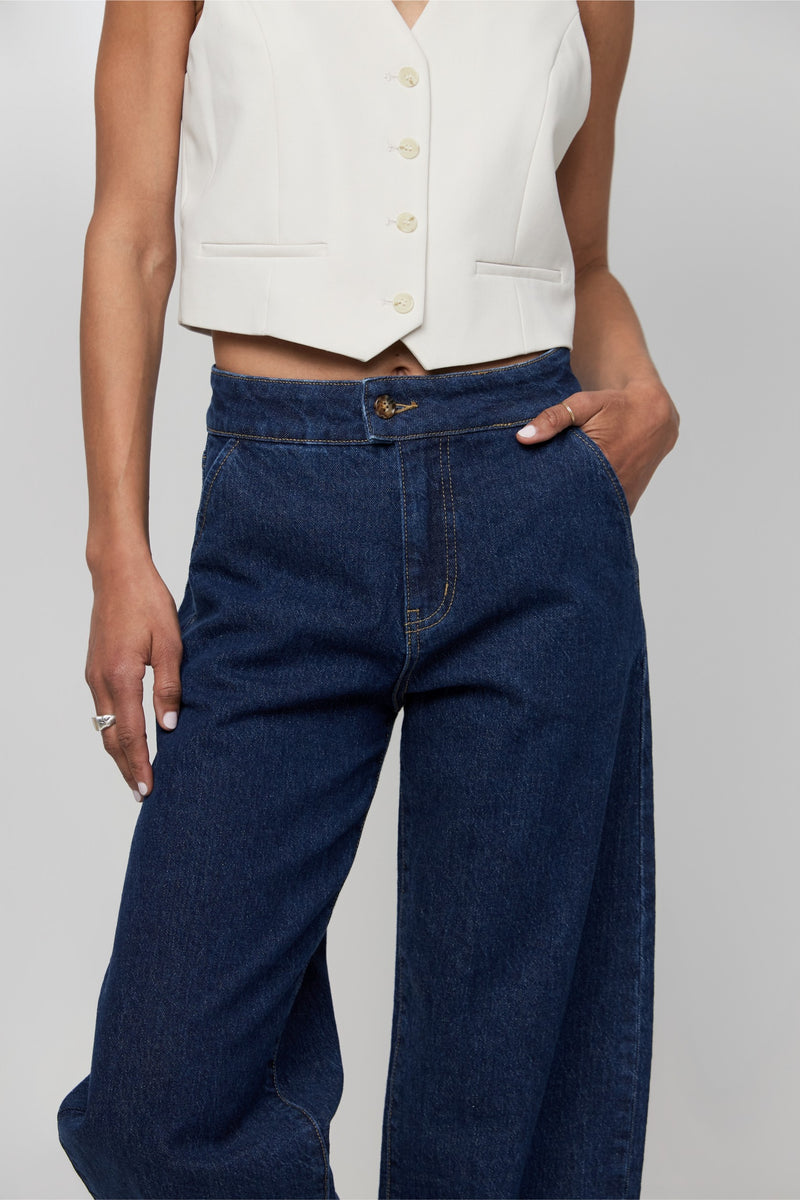 Video of high-rise barrel-leg jeans in dark indigo, showing front-tuck styling and the natural drape of the curved leg.