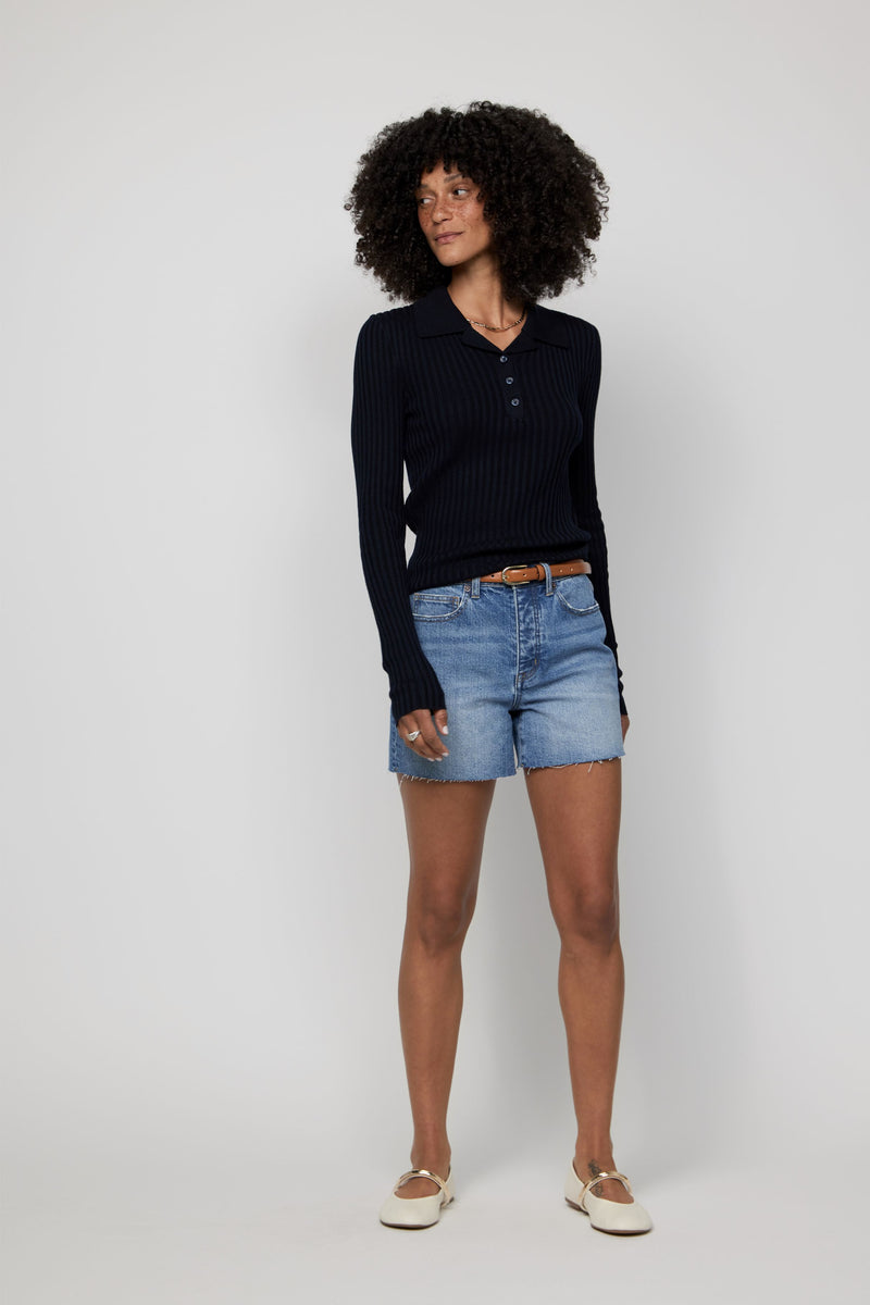 Video of model in high-rise denim shorts for women in a light blue wash styled with a black long-sleeve top.