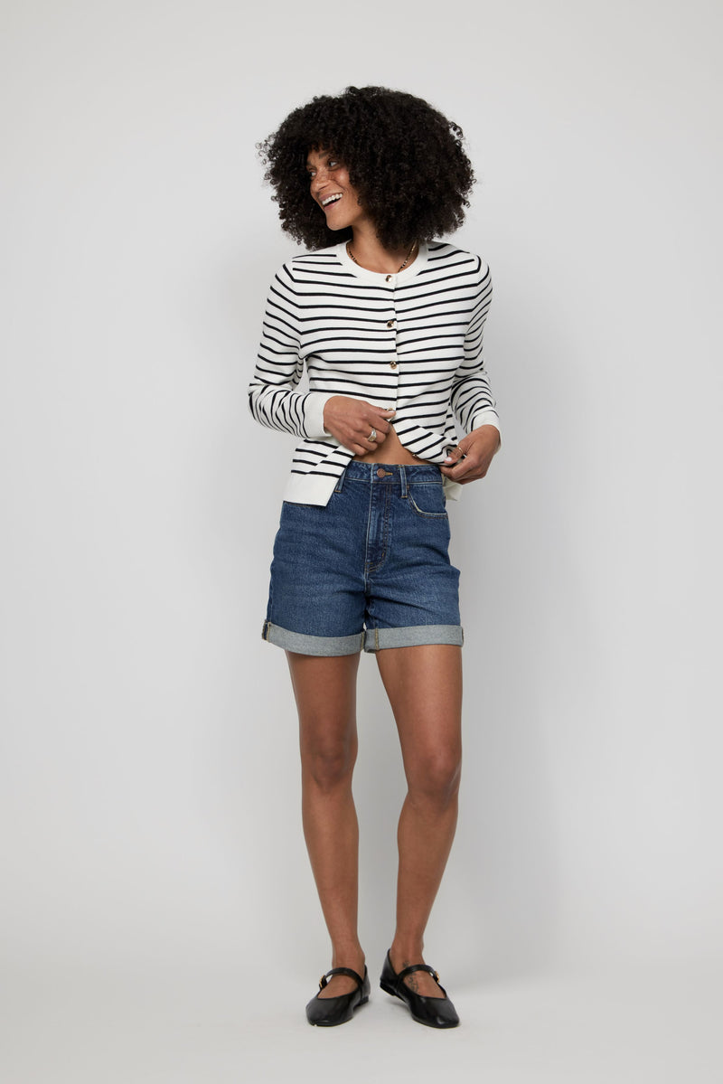 Video of woman styling high-rise dark wash denim shorts with a striped shirt and Mary Jane flats.