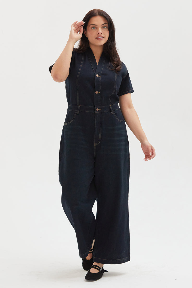 Plus-size model moving in a dark indigo denim romper, demonstrating its comfort and versatile everyday appeal.