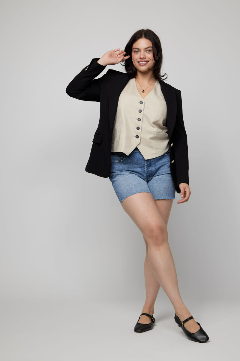 Video of plus-size woman modeling high-rise denim shorts in a vintage blue wash with a blazer and vest.