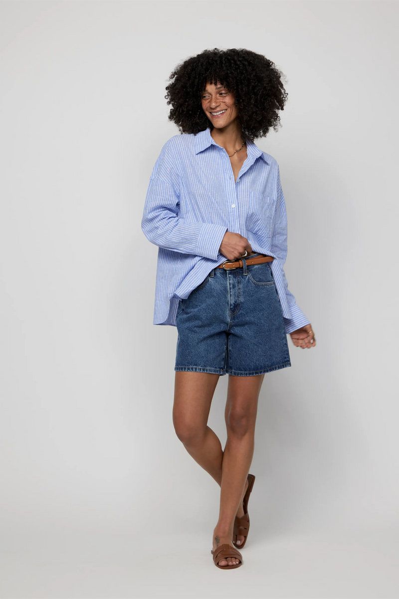 Video of high-rise dark denim shorts for women styled with a tucked-in shirt and sandals.