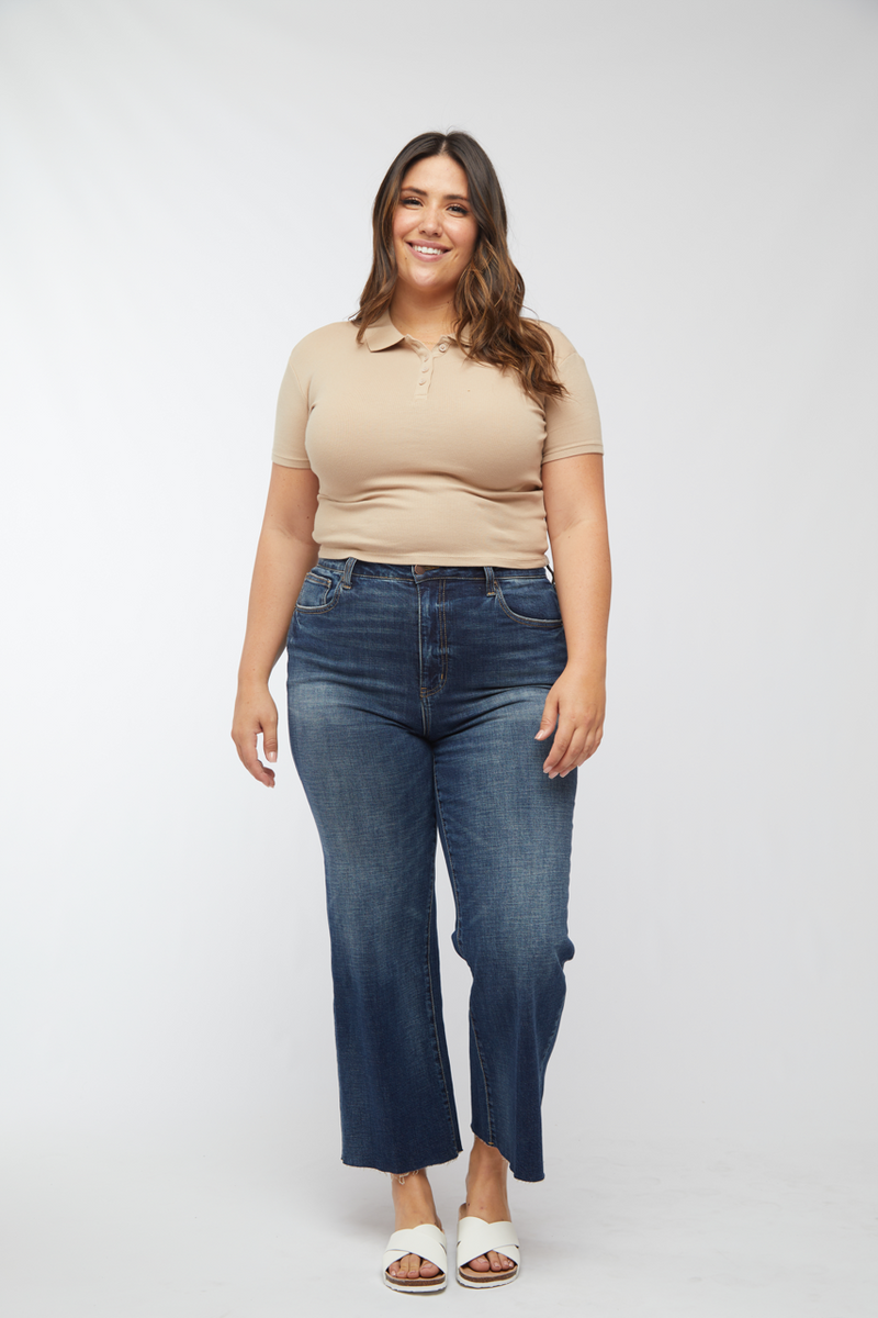 Plus-size model in dark wash high waisted wide leg cropped jeans, paired with a beige top, front view.