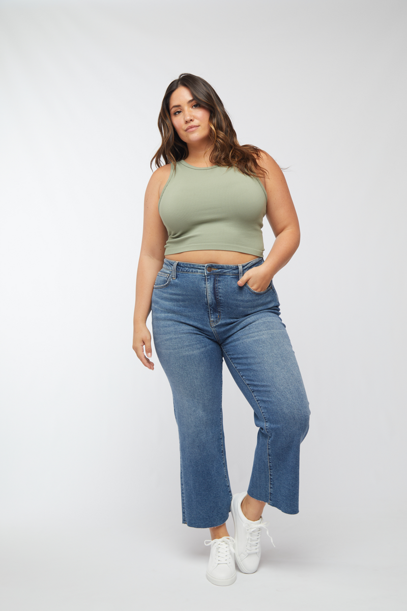 Plus-size model wearing light wash wide leg cropped jeans and a green tank top, front view showcasing the relaxed fit.