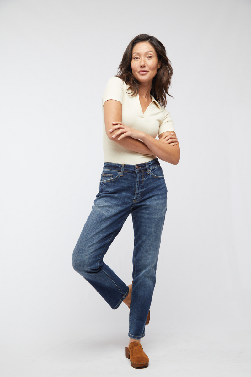 Front view of model in mid-rise relaxed fit jeans, paired with a cream-colored top and brown ankle boots.