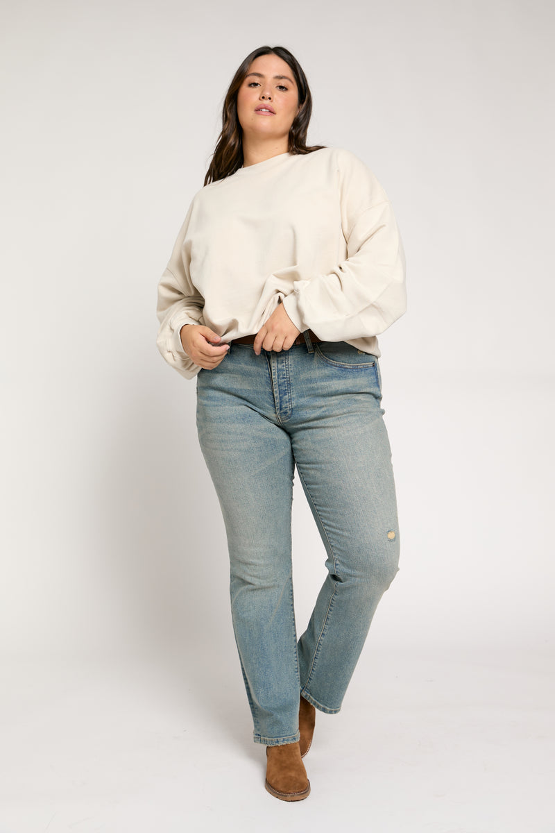 Plus-size model in front view wearing light vintage wash mid-rise straight-leg jeans paired with a beige sweater and boots.