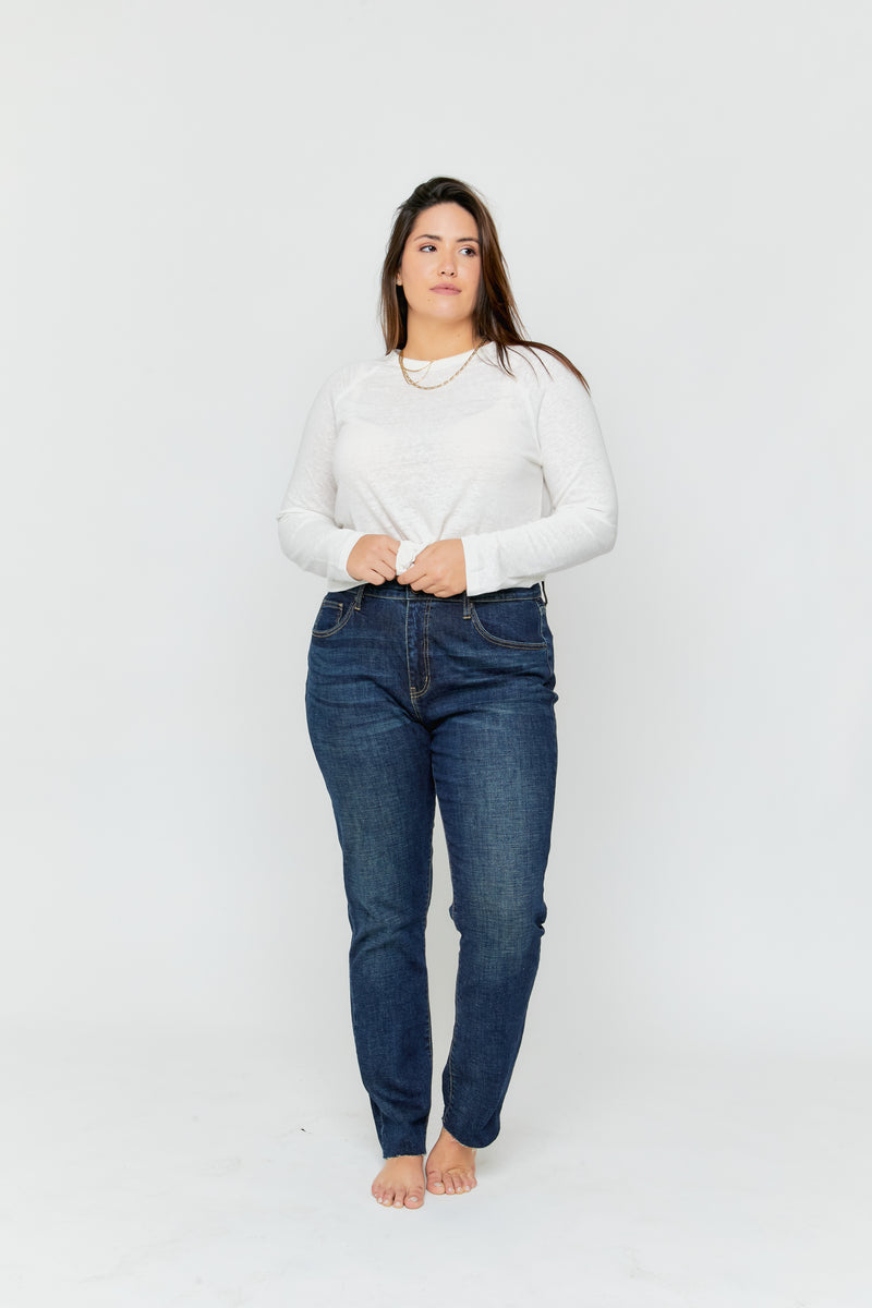 Plus-size model wearing high rise straight leg jeans in dark denim, paired with a white long-sleeve top, front view showing the relaxed fit.