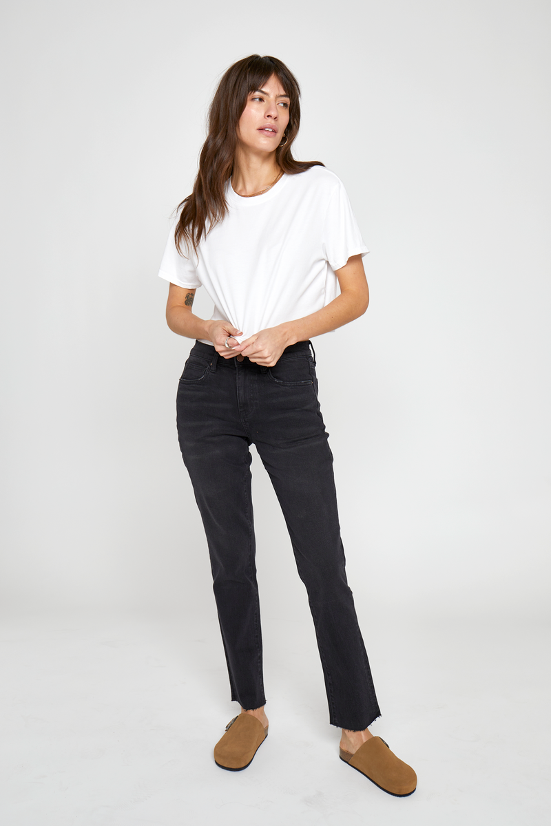 Model wearing high-rise tapered-leg jeans in a black wash, styled with a cropped white t-shirt and brown flats, showcasing a slim fit through the legs and flattering high-rise waist.