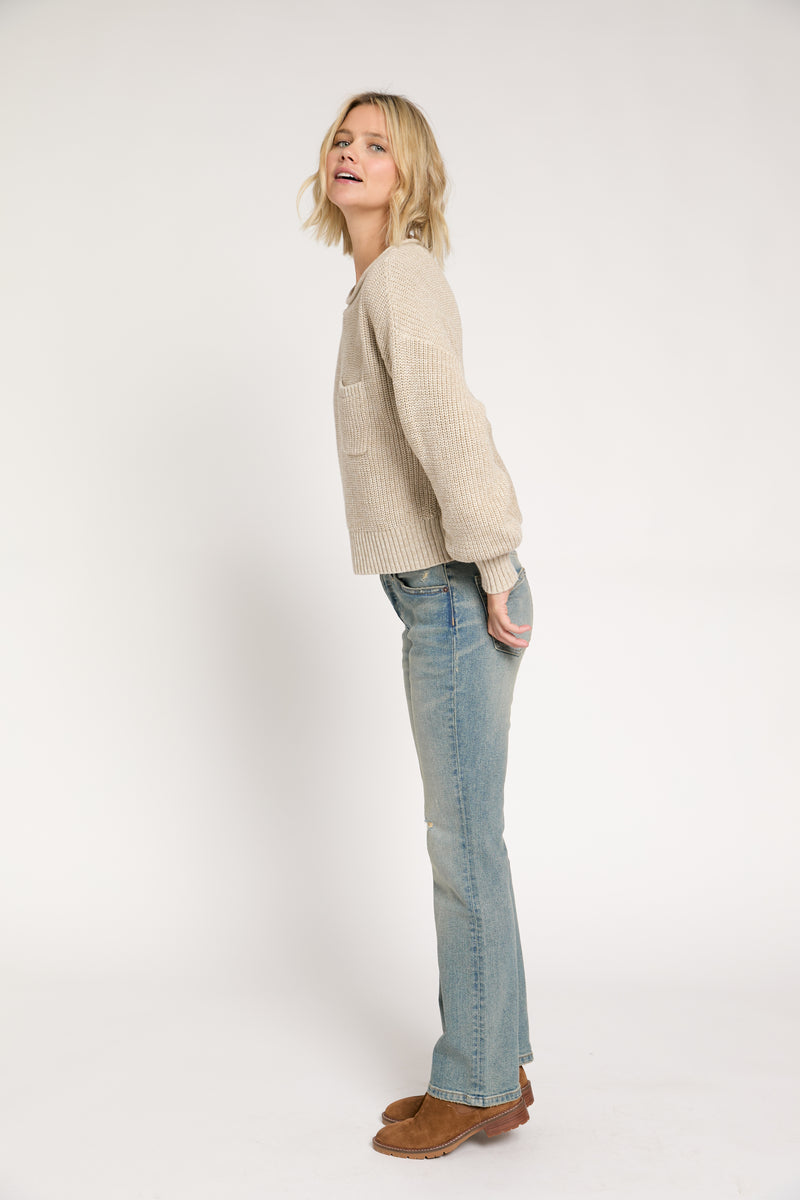 Model standing sideways in light vintage wash mid-rise straight-leg jeans paired with a beige knit sweater and brown boots.