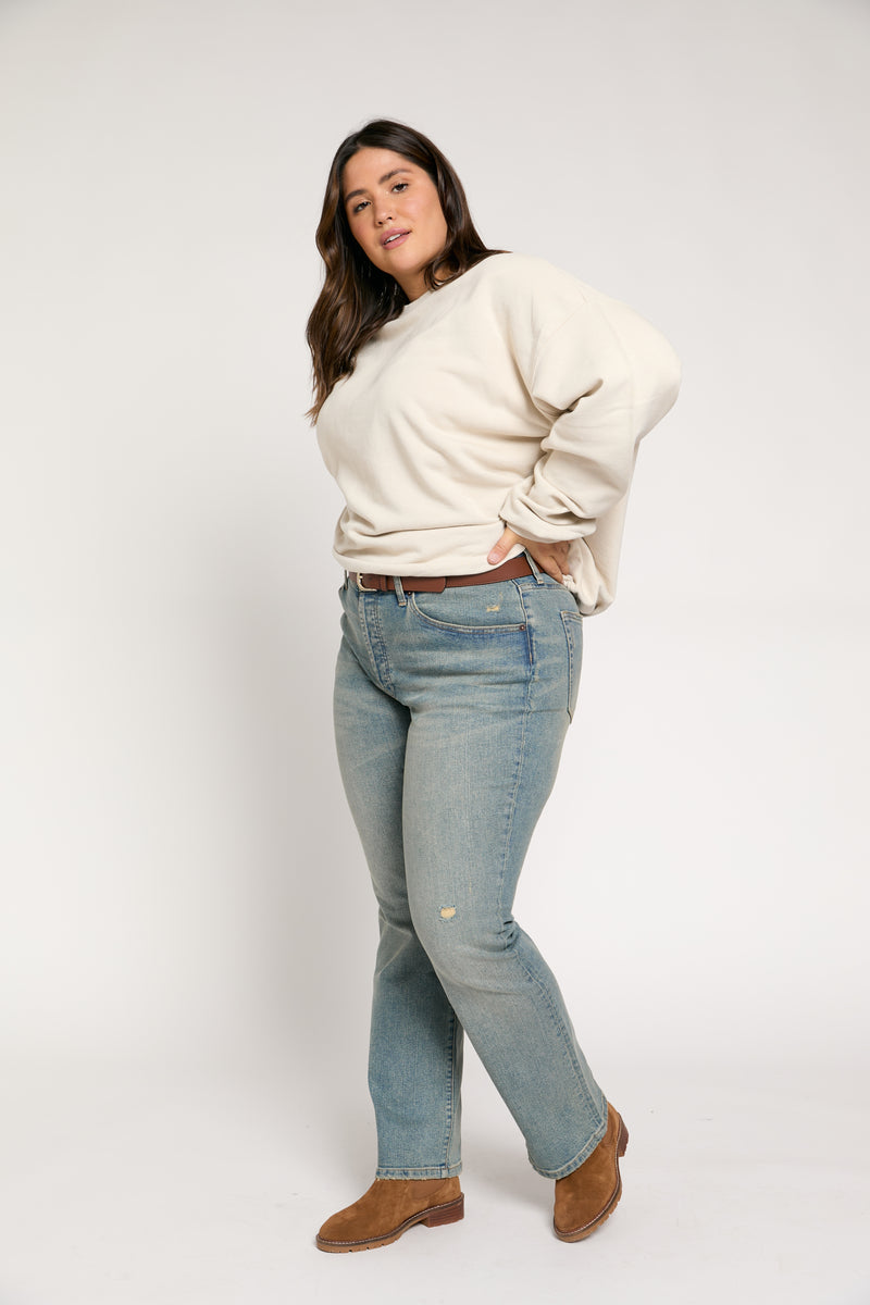Plus-size model in back view showing light vintage wash mid-rise straight-leg jeans, highlighting the flattering fit and stretch.