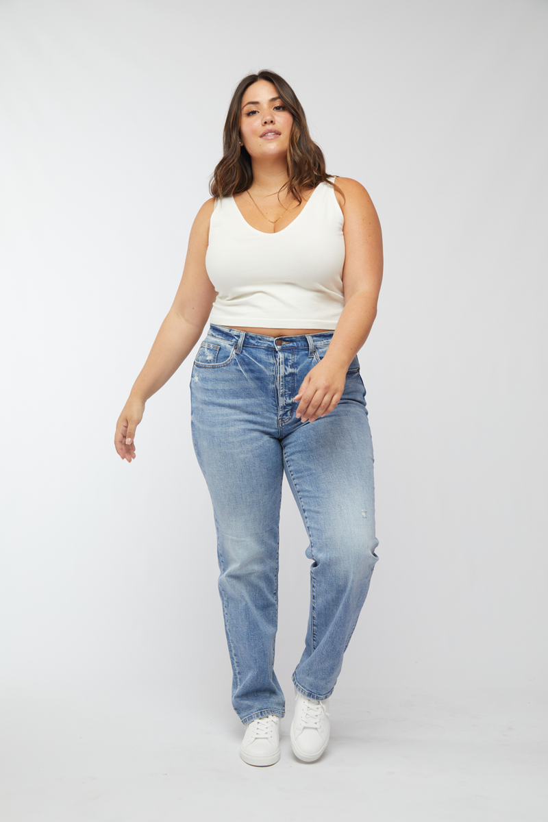 Plus-size model confidently posing in high rise vintage jeans, paired with casual white sneakers, highlighting the light denim and relaxed fit.