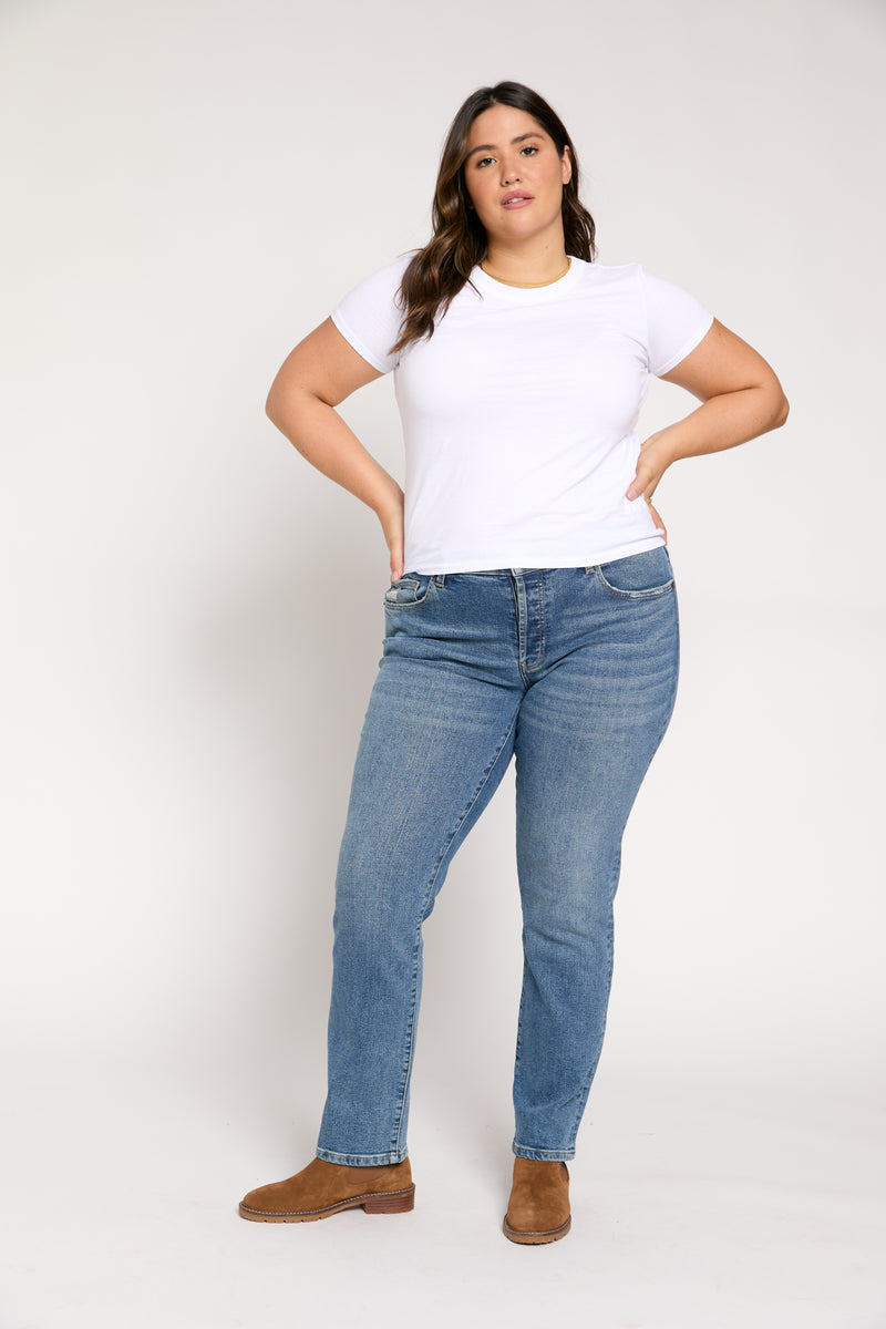 Full-length front shot of plus-size straight leg high-rise jeans in classic blue denim, styled casually with a white tee and brown boots.