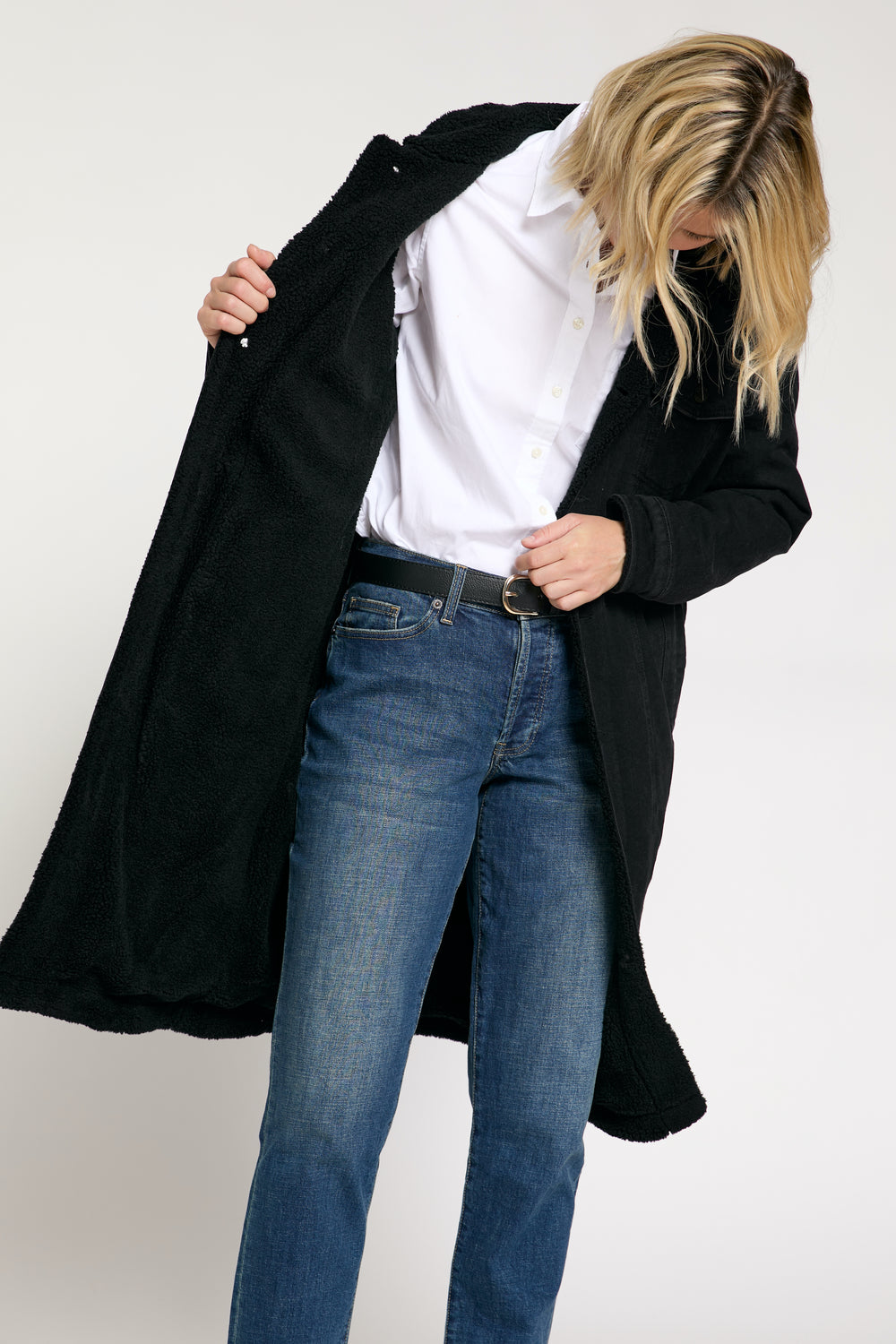 The model opens the long sherpa coat to reveal the interior sherpa lining, showing off its cozy and warm details.