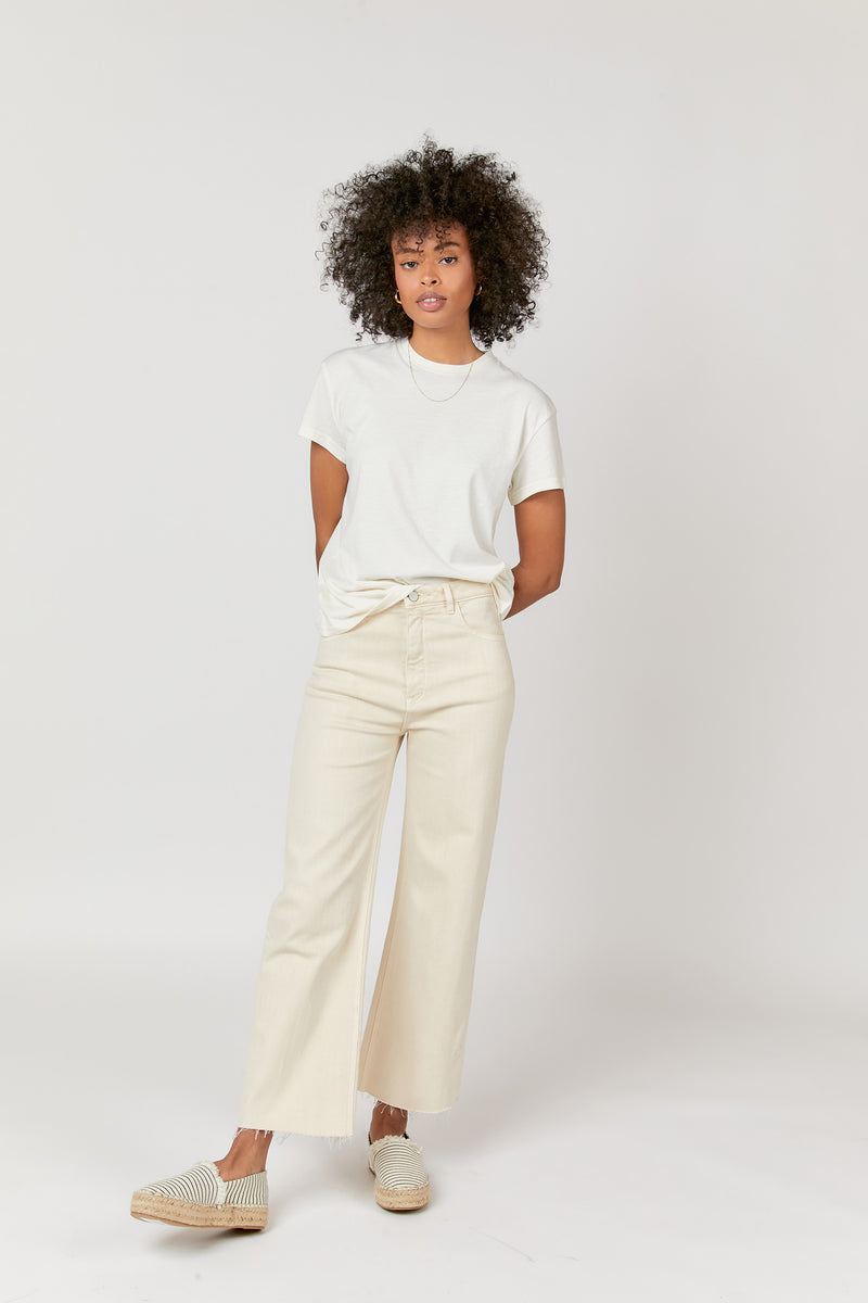 Model wearing ecru denim cropped wide leg jeans with a white t-shirt, front view highlighting the relaxed fit.