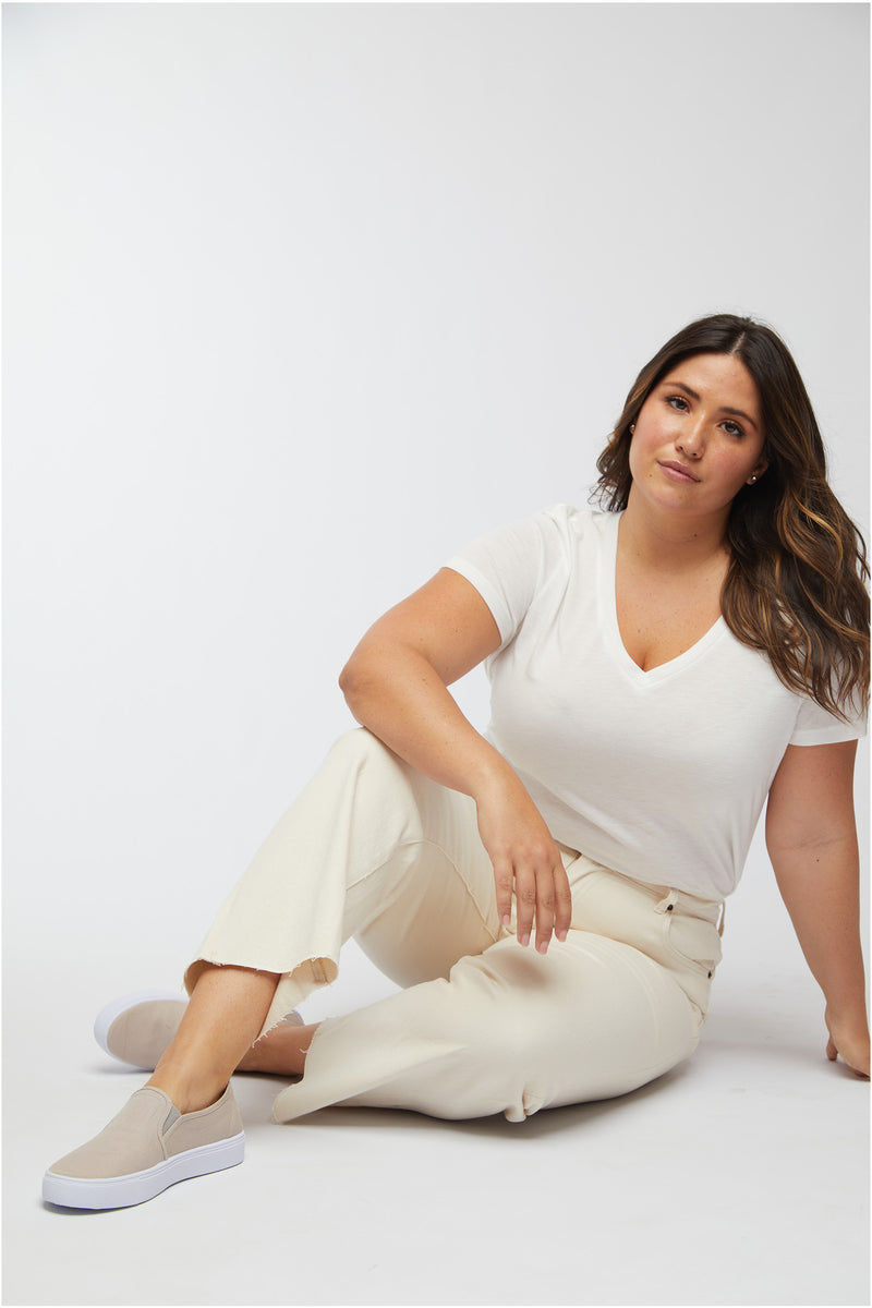 Plus-size model sitting confidently in ecru denim jeans, paired with a white tee, showing the comfortable and stylish look.