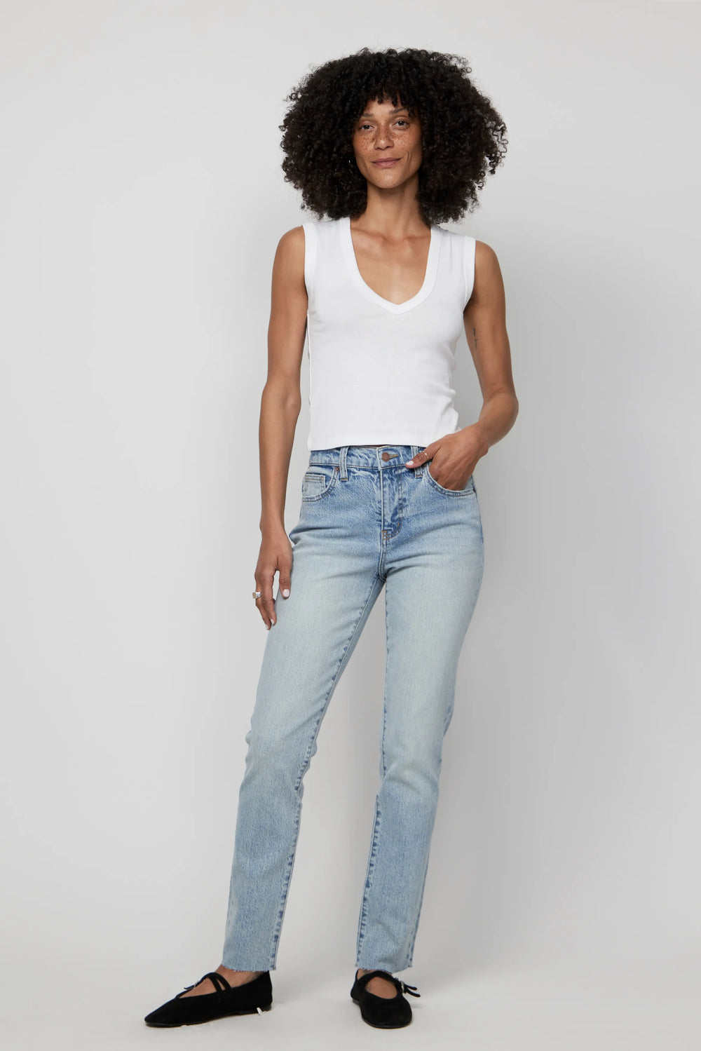Woman wearing high-rise relaxed fit light wash jeans and a white tank top, front-facing view.