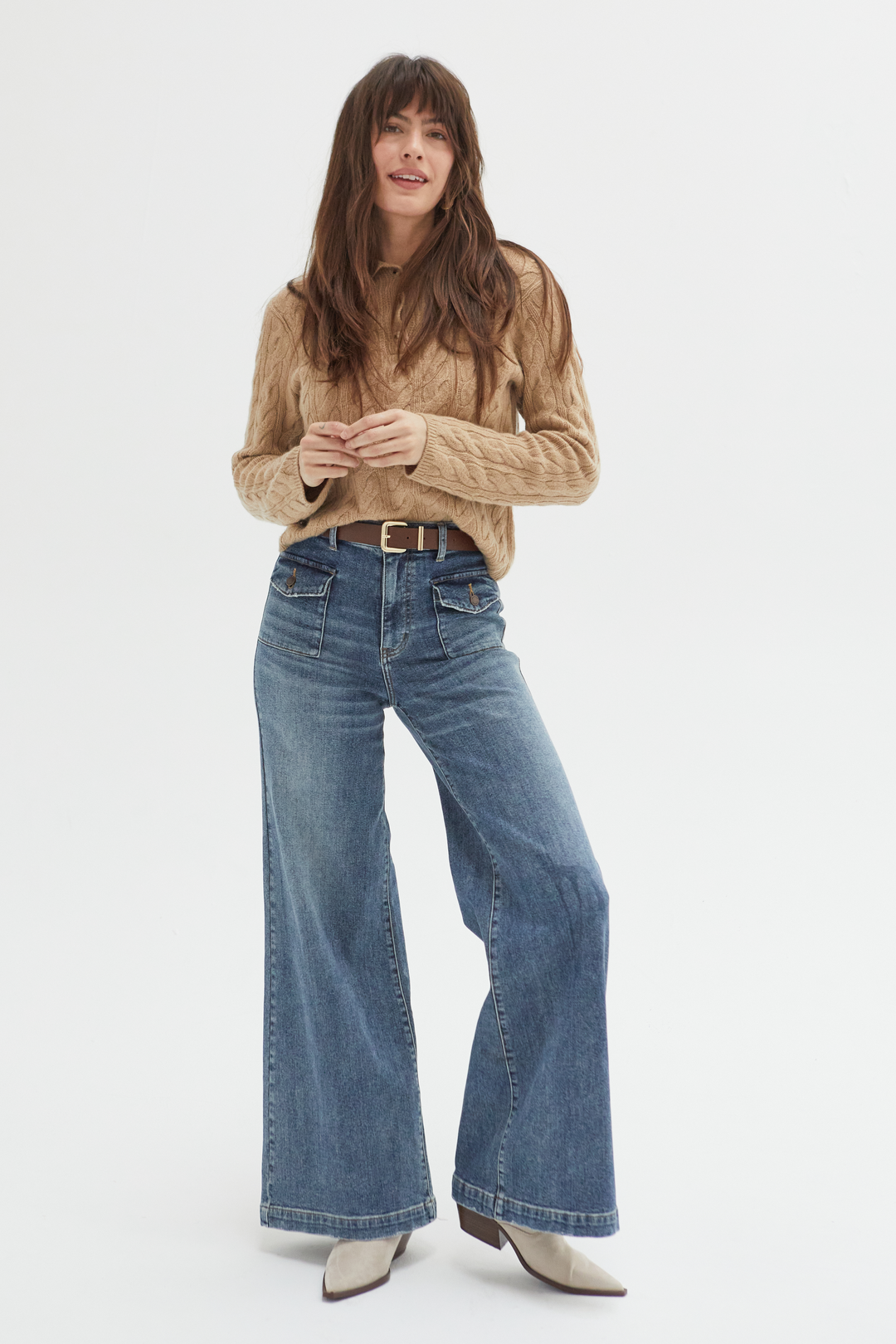 Model wearing high-rise wide-leg jeans in a medium blue wash, styled with a tan cable-knit sweater and beige boots, showcasing a relaxed fit and full-length wide-leg silhouette.