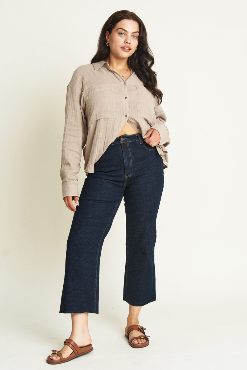 Plus size model in high rise cropped jeans wearing a brown button up top.