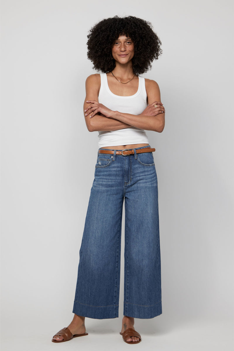 Plus-size woman wearing high-rise wide-leg cropped jeans in medium blue denim with a white tank.