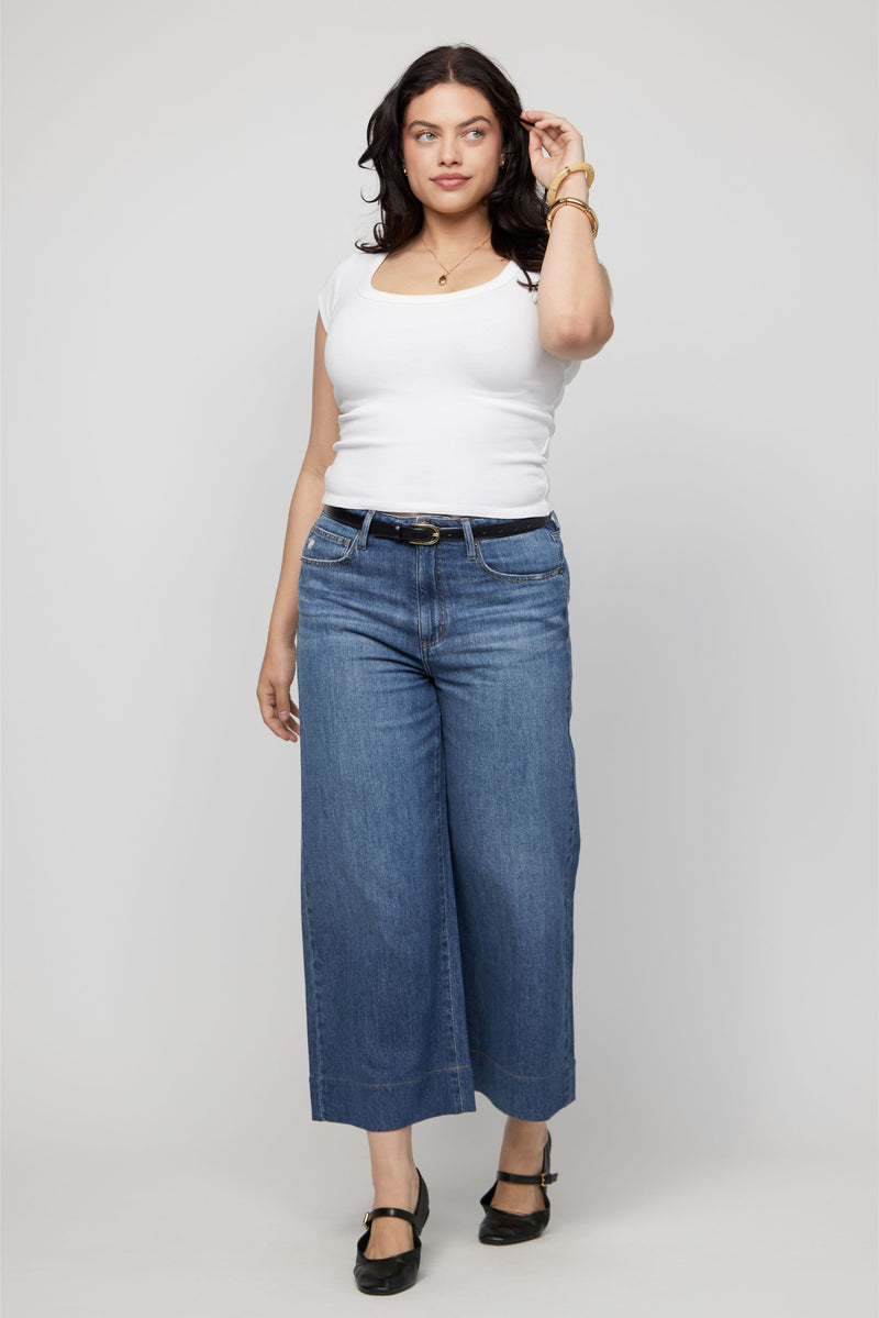 Woman wearing high-rise cropped wide-leg jeans in medium-dark indigo denim with a white tank top.