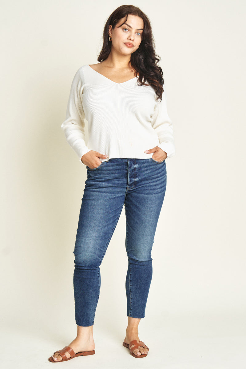 Plus-size model facing front in dark wash skinny jeans, paired with an off-shoulder white sweater.
