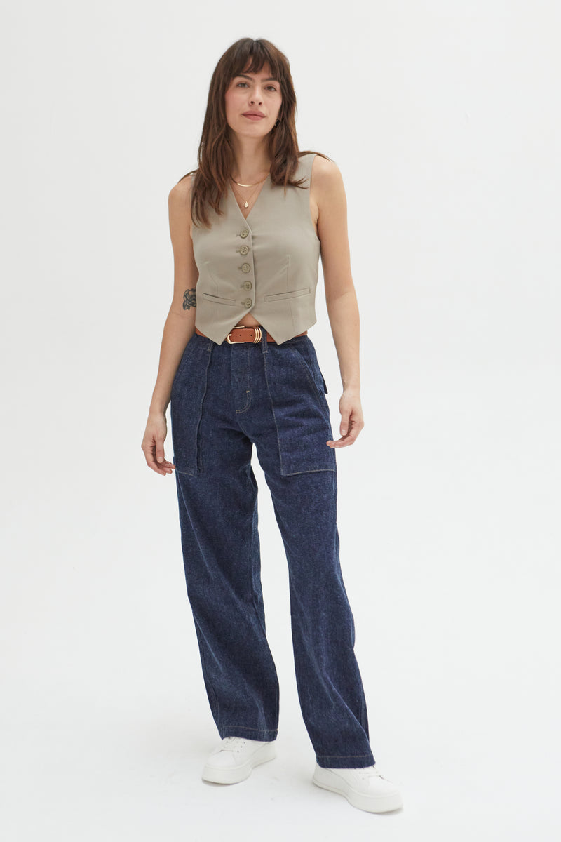 Model wearing trouser jeans in a dark indigo wash, styled with a beige tank and white sneakers, showcasing a relaxed fit and wide leg with front pocket detailing.
