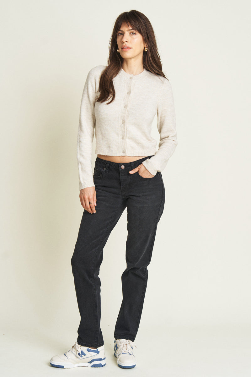 Model wearing low-rise jeans in a black wash, styled with a cream cardigan and white sneakers, showcasing a relaxed fit and straight-leg silhouette.
