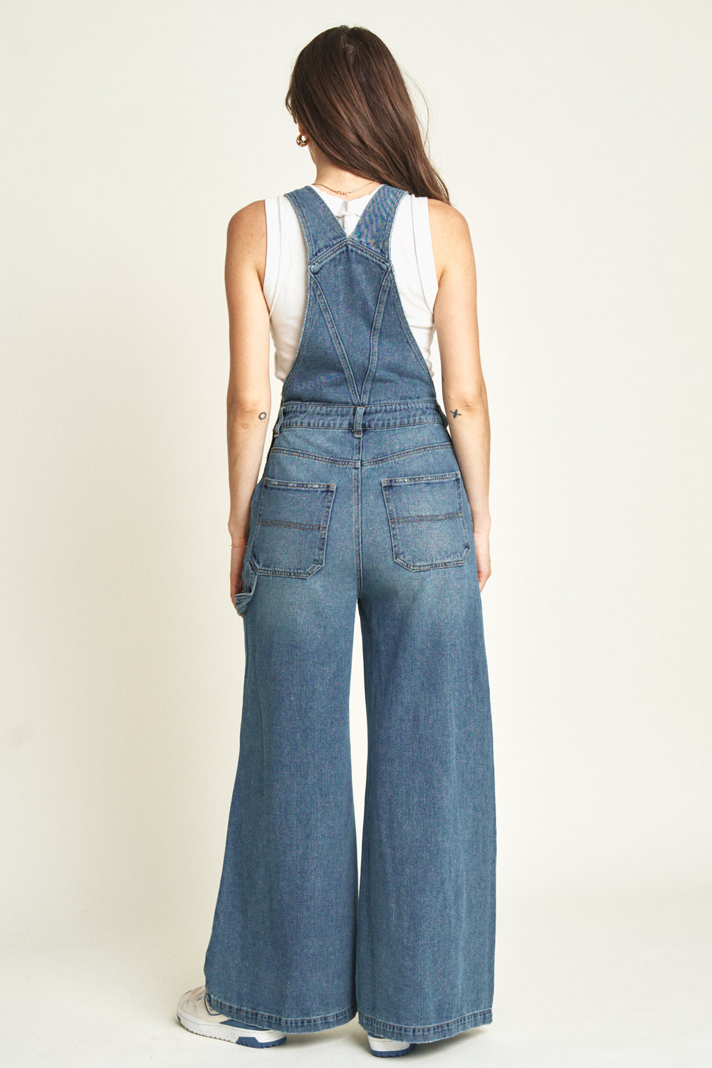 Back view of a model in wide-leg denim overalls, emphasizing the clean back pockets, adjustable straps, and flowing wide-leg silhouette.