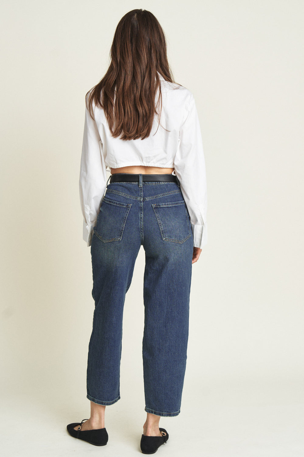 Back view of model in high rise barrel jeans, showing the relaxed fit and vintage blue wash, styled with black flats.
