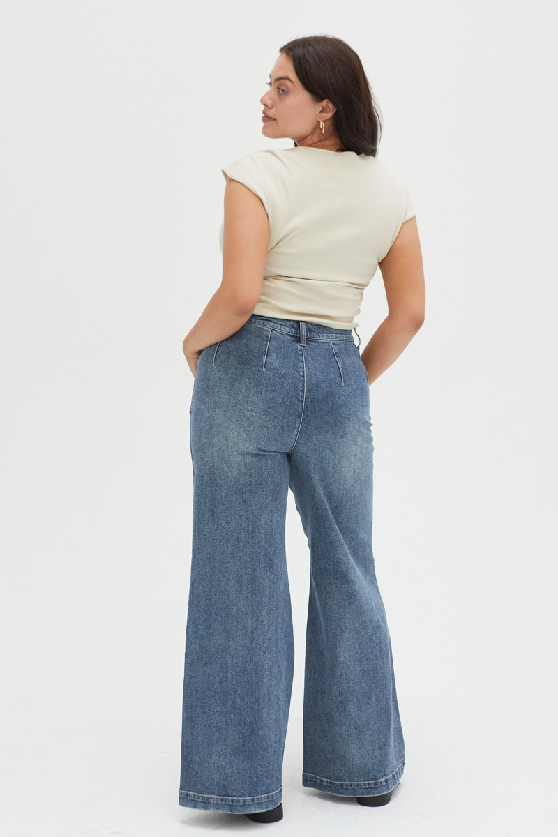 Back view of a curvy model in medium blue high-rise wide-leg jeans, emphasizing the tailored design and flattering fit through the hips and waist.