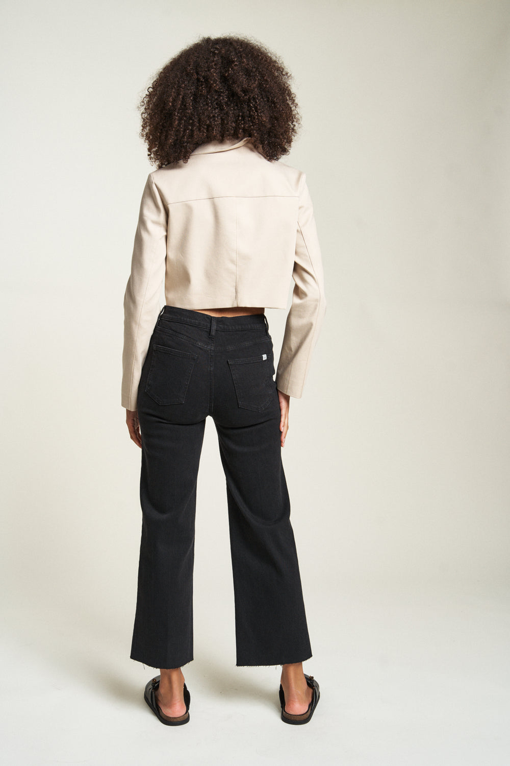 Back view of model in black wash wide leg cropped jeans, styled with black loafers, showcasing the high-rise fit.	