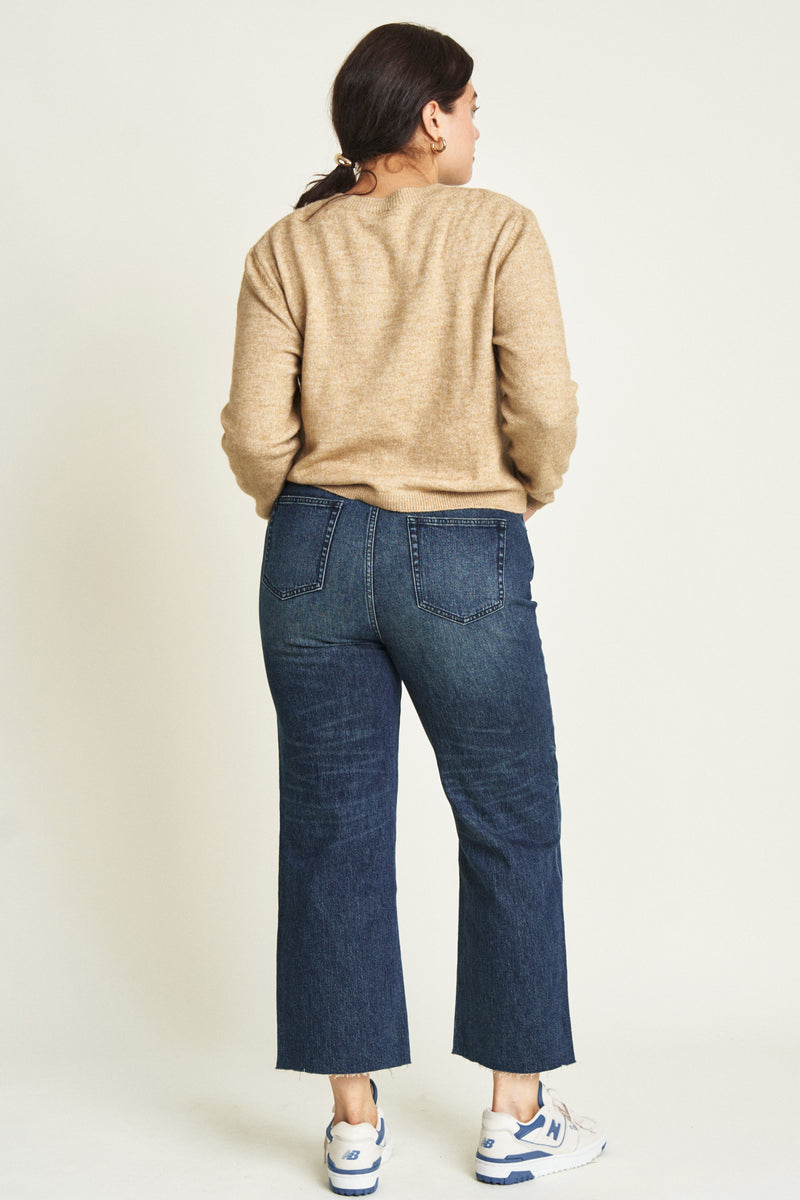 Back view of a curvy model in dark blue ankle crop jeans, emphasizing the tailored fit through the hips and clean pocket details.