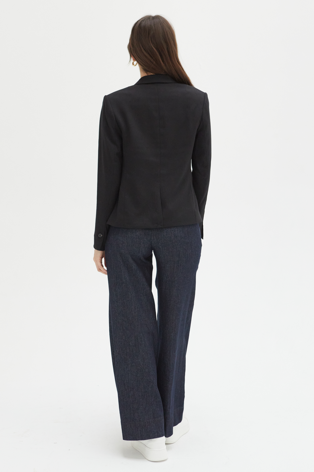 Back view of a model in dark wash low-rise wide-leg pants, emphasizing the tailored pleats and clean seam detailing.