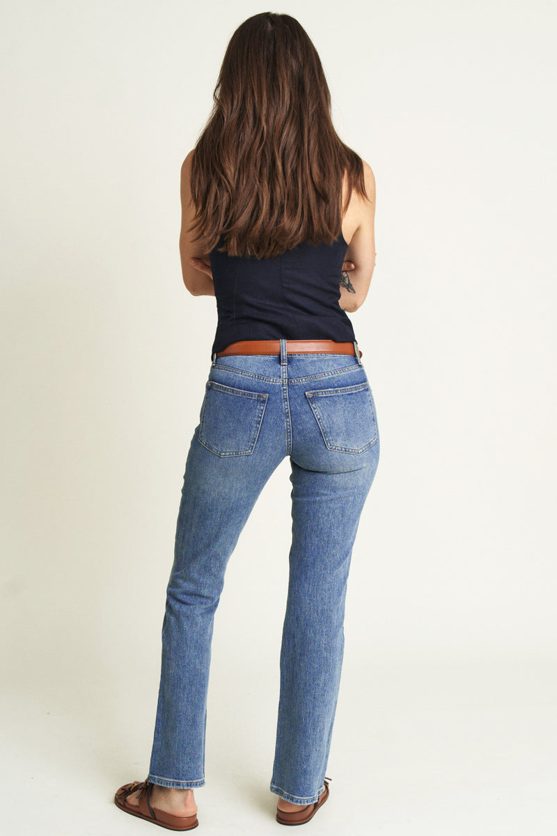 Woman turned backward in light wash mid-rise bootcut jeans, showcasing back pockets and relaxed fit for a timeless, vintage vibe.