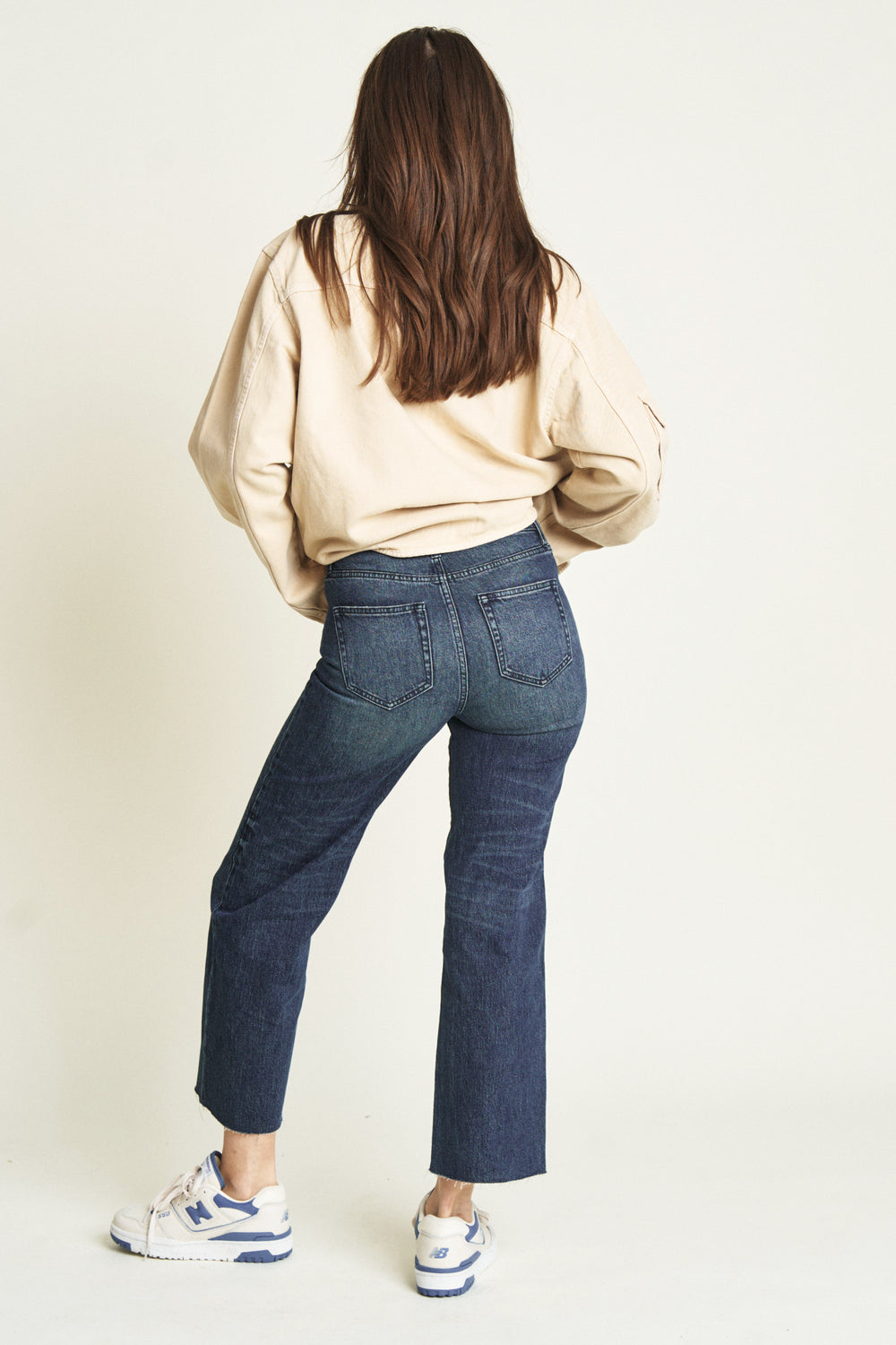 Back view of a model in dark blue ankle crop jeans, highlighting the tailored fit and clean pocket design.
