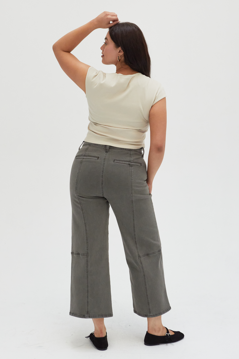 Back view of a plus-size model in olive wide-leg ankle crop jeans, highlighting the unique panel stitching and comfortable fit.
