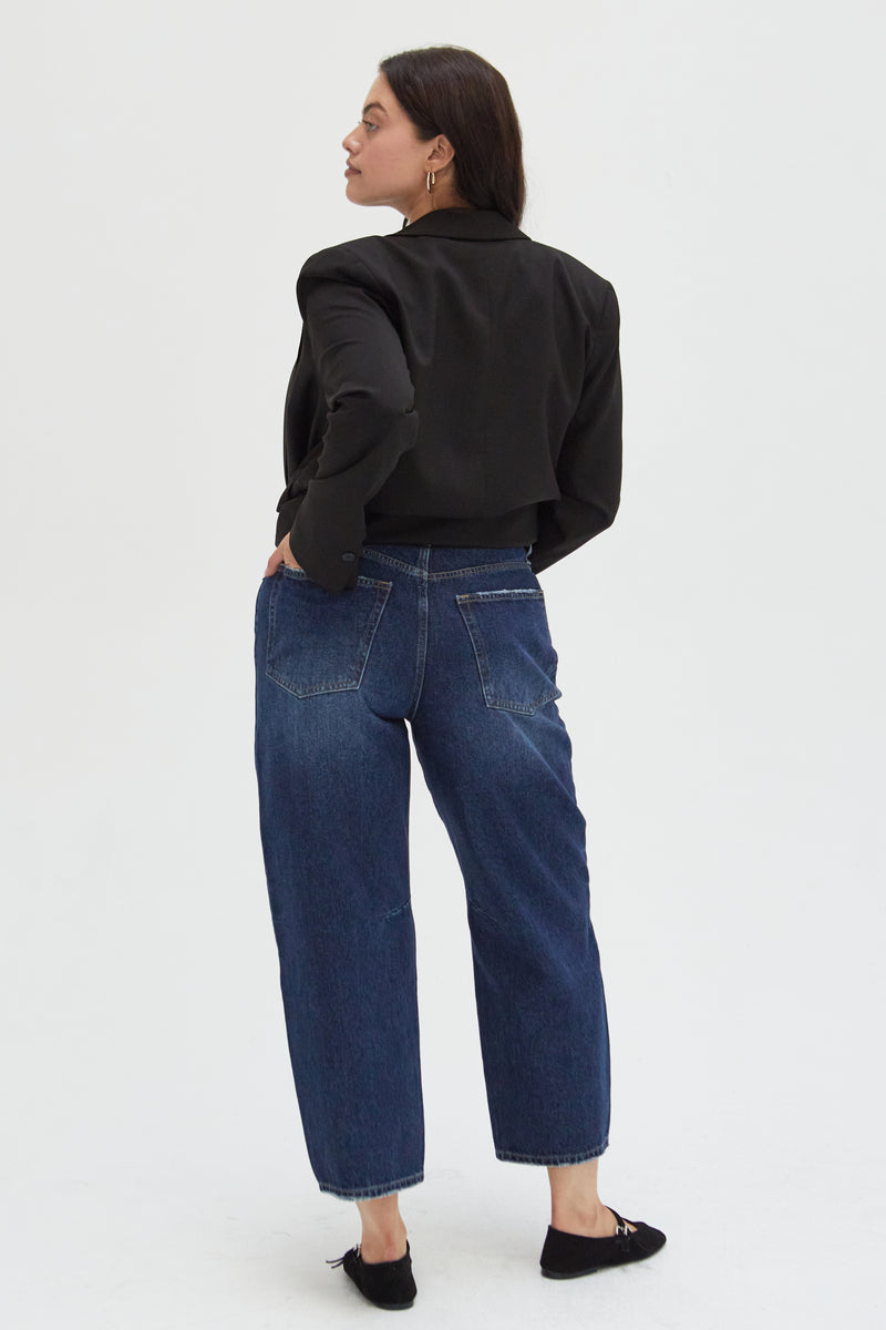 Back view of a plus-size model in dark indigo high-rise barrel jeans, emphasizing the structured silhouette and relaxed fit.
