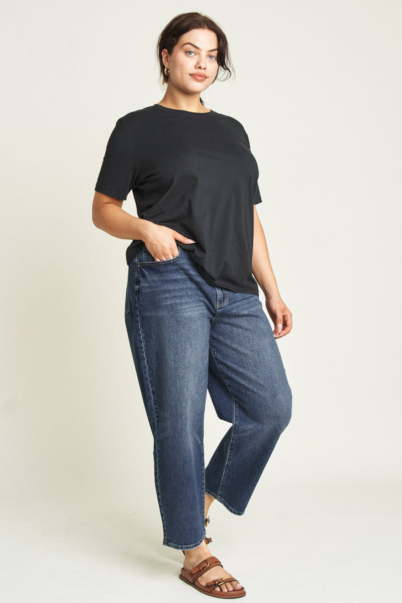 Close-up of high rise curved leg jeans, highlighting the dark blue denim texture and button closure.