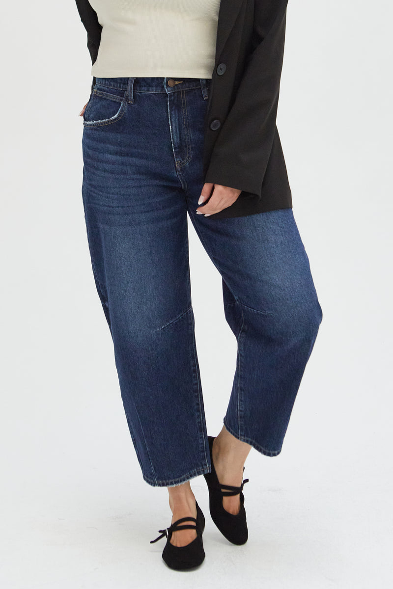 Close-up of high-rise barrel jeans on a plus-size model, highlighting the curved leg design and sustainable denim material.