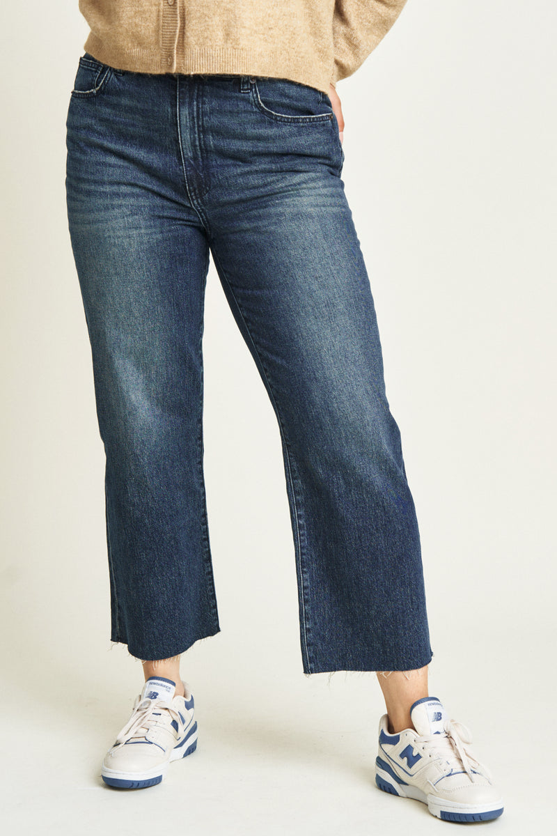 Close-up of dark blue ankle crop jeans, highlighting the durable denim fabric, structured seams, and cropped hemline.