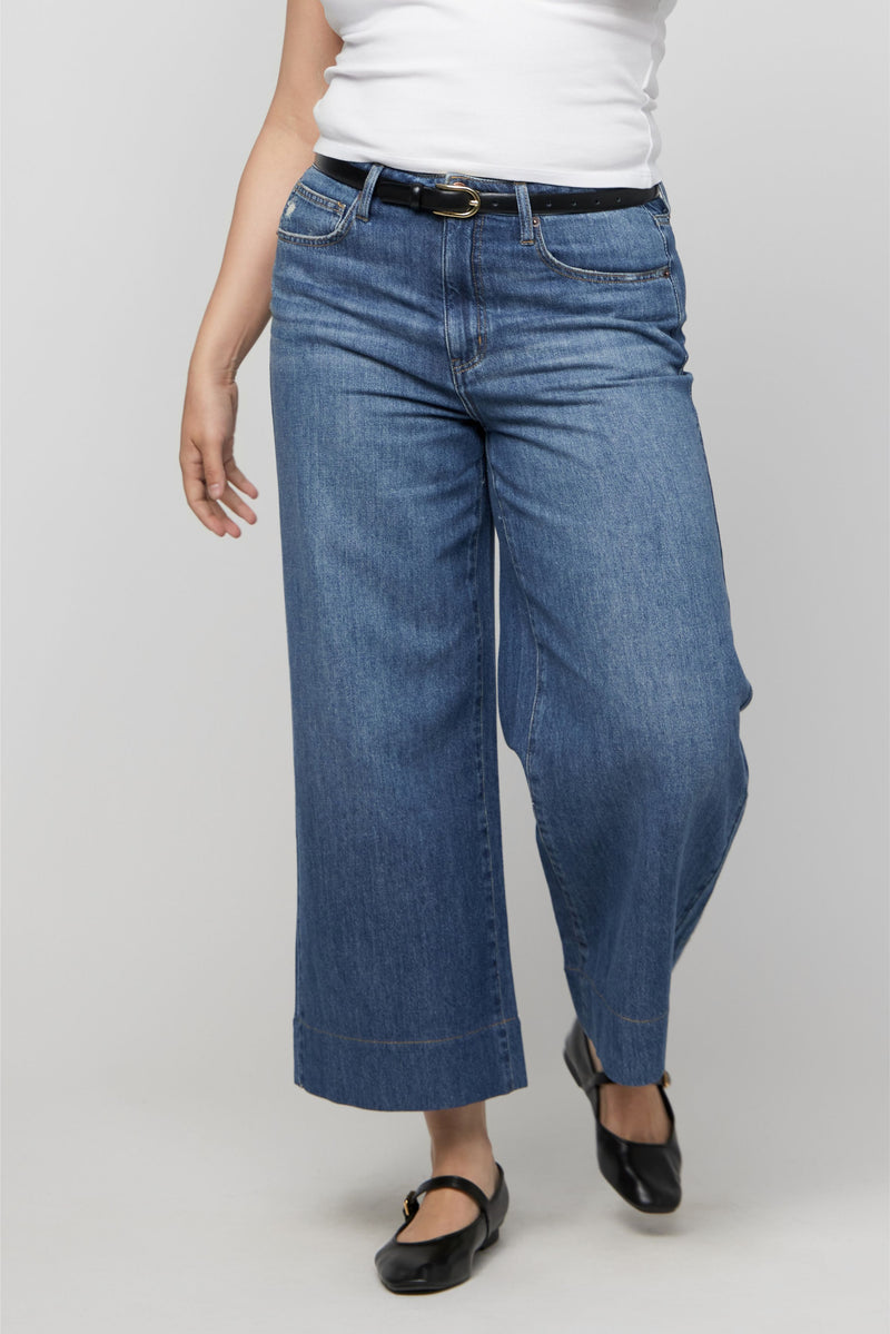 Close-up of high-rise waistband and pocket detail on cropped wide-leg jeans in a rich indigo wash.