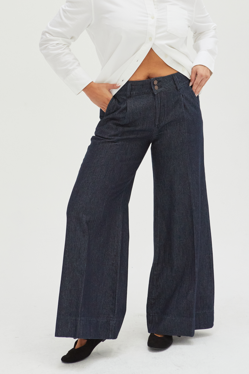 Close-up of dark wash wide-leg pants, highlighting the structured pleats, soft fabric, and low-rise waistband.
