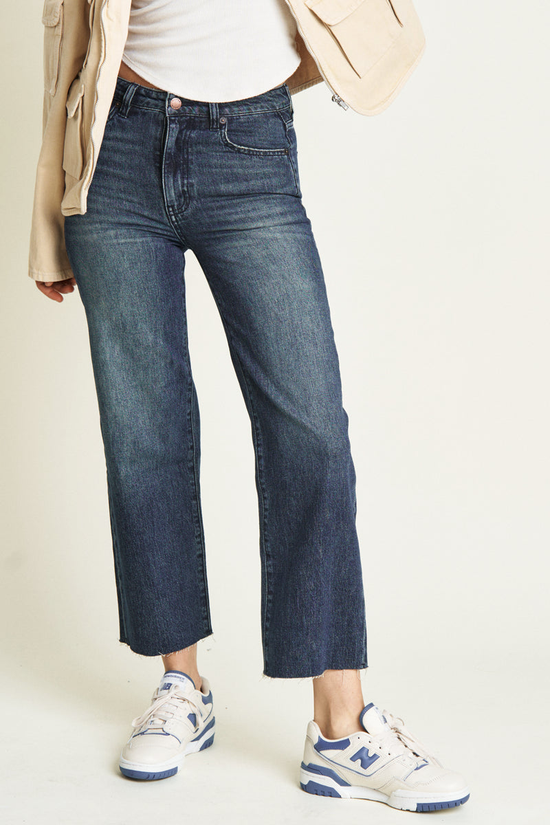 Close-up of dark blue ankle crop jeans, emphasizing the durable fabric, structured seams, and cropped hem.
