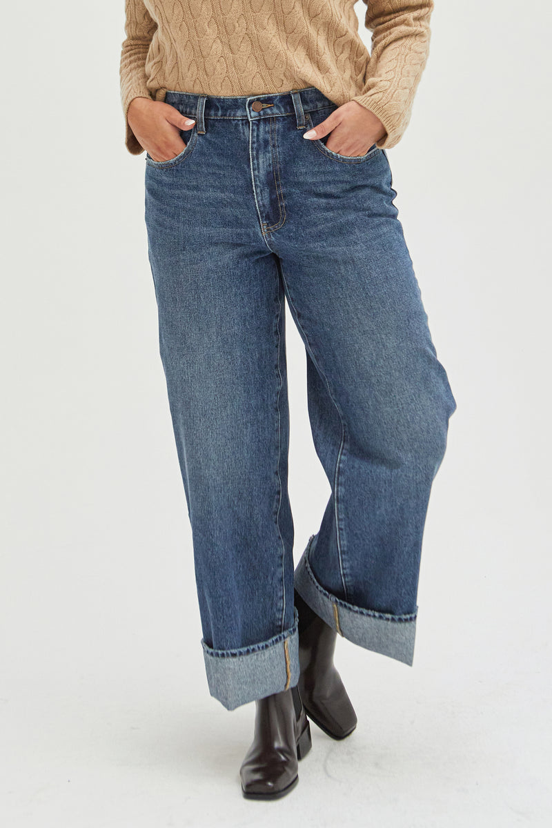 Close-up of mid-rise wide-leg jeans, highlighting the structured waistband, deep blue wash, and cuffed hem for a timeless, relaxed fit.